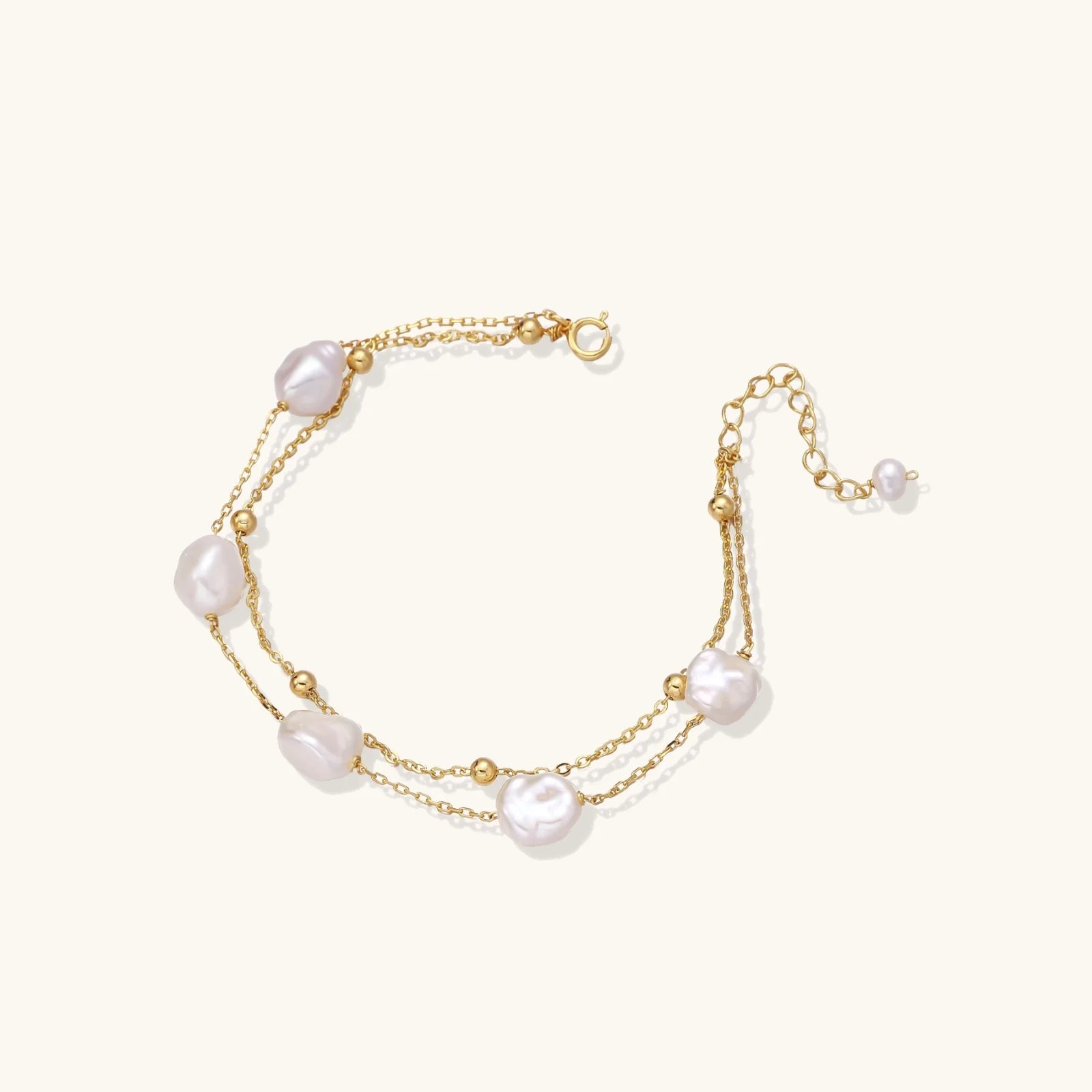 Double-strand gold bracelet with irregular baroque pearls and smooth freshwater pearls on cream background.