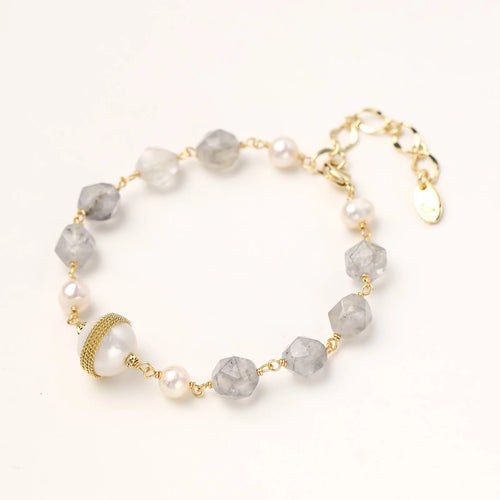 Bracelet with cloudy quartz beads, freshwater pearls, and gold-wrapped baroque pearl centerpiece on white background.