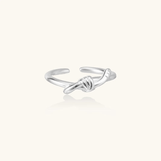 Delicate rhodium-plated silver ring with elegant knot design on cream background, adjustable band style