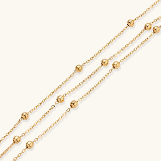Three-strand gold-plated bracelet with clustered ball beads and adjustable clasp on cream background
