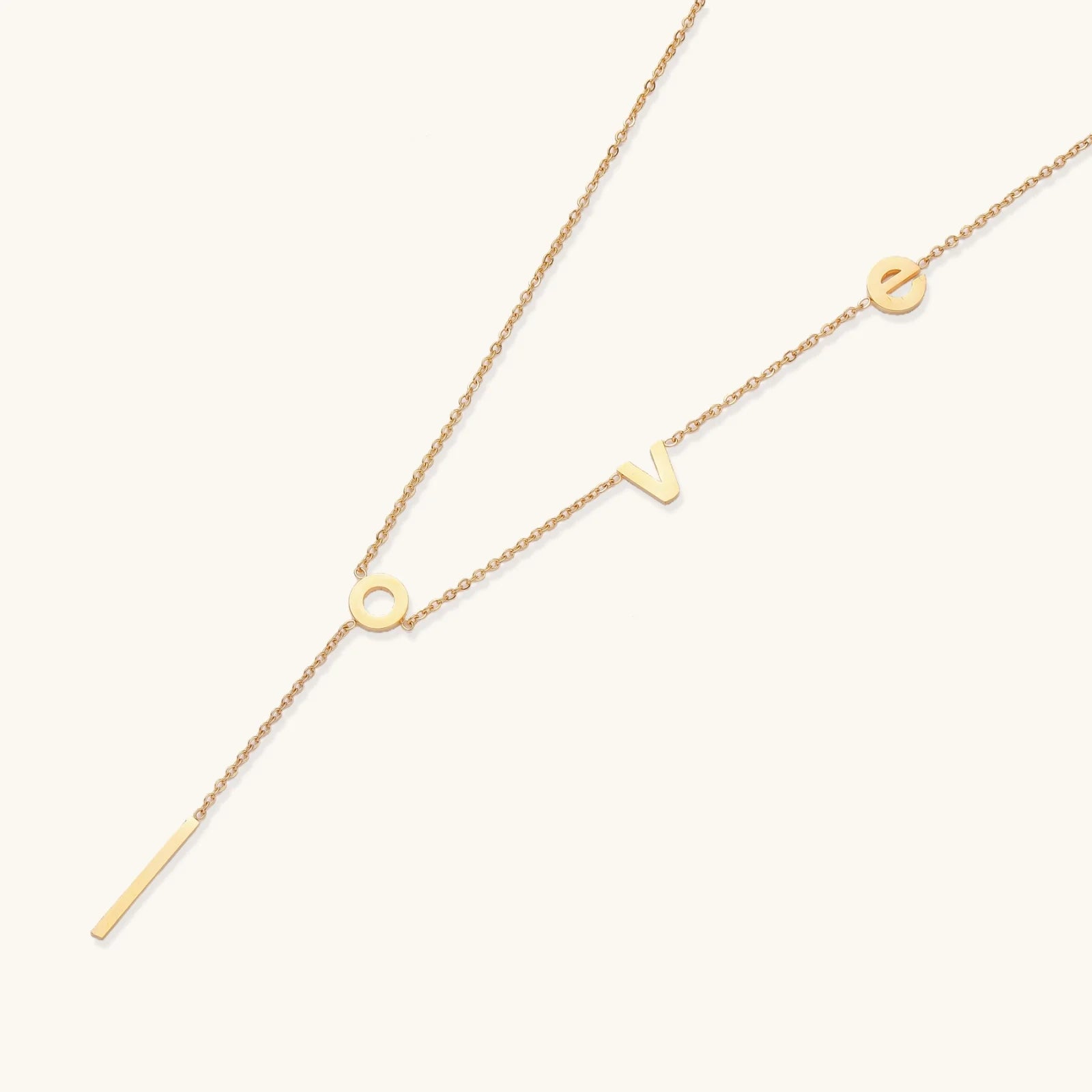 Gold Y-shaped necklace with L-O-V-E letter charms and vertical bar pendant on delicate chain against cream background